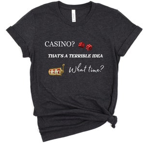 May include: Dark gray t-shirt with white text that reads "Casino? That's a terrible idea. What time?"  The shirt also features a graphic of a slot machine and two red dice.
