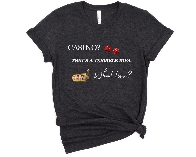 May include: Dark gray t-shirt with white text that reads "Casino? That's a terrible idea. What time?"  The shirt also features a graphic of a slot machine and two red dice.