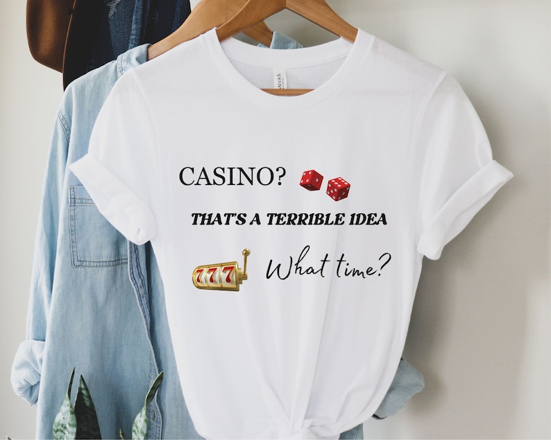 May include: White t-shirt with the text "CASINO? THAT'S A TERRIBLE IDEA What time?" and a graphic of dice and a slot machine.