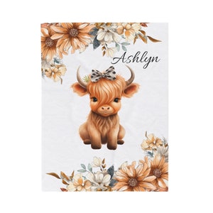 May include: A cute brown and white Highland cow with a black and white bow on its head, surrounded by orange and white flowers. The name "Ashlyn" is written in black cursive above the cow.