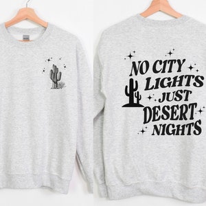 Może przedstawiać: Szara bluza z nadrukiem kaktusa i gwiazd na przodzie i napisem "NO CITY LIGHTS JUST DESERT NIGHTS" na plecach.