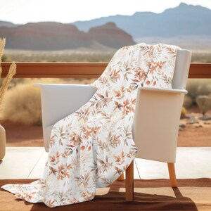 May include: A white chair with a throw blanket featuring a brown and white floral pattern. The chair is on a patio with a view of a desert landscape.