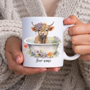 May include: White ceramic mug with a colorful illustration of a Highland cow taking a bath in a white bathtub with flowers around the rim. The text "Your name" is printed on the mug.