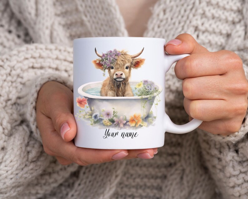 May include: White ceramic mug with a colorful illustration of a Highland cow taking a bath in a white bathtub with flowers around the rim. The text "Your name" is printed on the mug.