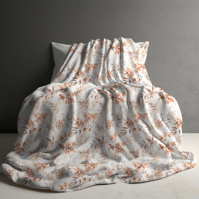 May include: A white throw blanket with a brown and orange floral pattern. The blanket is folded and draped over a white pillow.