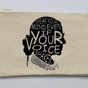 May include: A beige canvas zippered pouch with a black silhouette of a woman's face. The silhouette is filled with the text "Speak your mind even if your voice shakes."