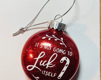 May include: Red glitter Christmas ornament with white text that reads "IT'S NOT GOING TO Luck ITSELF" and a candy cane graphic. The ornament has a silver string for hanging.