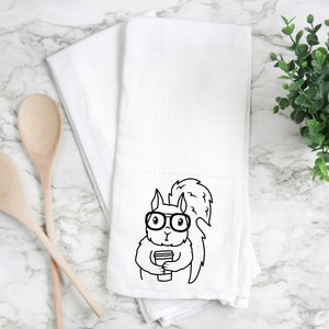 May include: White kitchen towel with a black and white illustration of a squirrel wearing glasses and holding a cup of coffee.