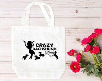 May include: White tote bag with black silhouette of a woman and dachshunds. The text "Crazy Dachshund Lady" is printed on the bag.
