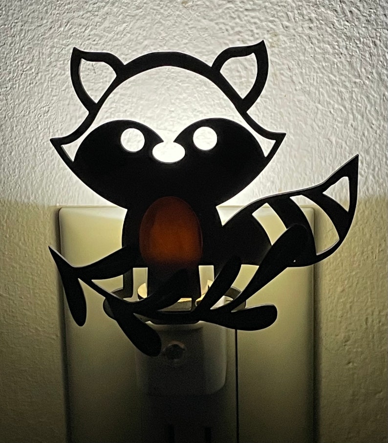 May include: A black silhouette of a raccoon with a light bulb in its belly, plugged into an outlet. The raccoon is holding a branch in its paws.
