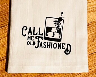 May include: White kitchen towel with black text that reads "Call me old fashioned" and a black silhouette of an old fashioned cocktail glass with a lemon wedge and a cherry.
