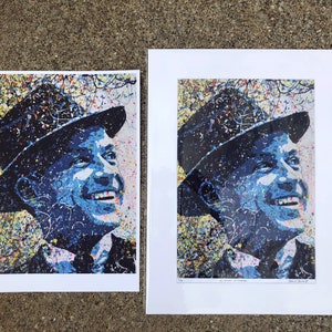 May include: A colorful, abstract portrait of a man wearing a hat. The image is made up of a variety of colors, including blue, yellow, and white. The man is smiling and looking up. The image is printed on a white background.