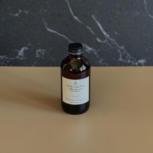 May include: A brown glass bottle with a black lid and a white label that reads "THE GROVE" with a small tree logo and the text "BOOKEND CANDLE CO."