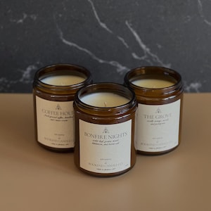 May include: Three amber glass candle jars with labels. The labels are white with black text and a small tree graphic. The candle scents are "Coffee House", "Bonfire Nights", and "The Grove".