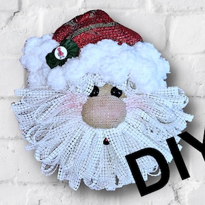 以下が含まれることがあります： DIYクリスマスリース。サンタクロースの顔は、麻布と白いメッシュで作られています。リースは、赤と緑の格子縞の帽子と白いポンポンで飾られています。