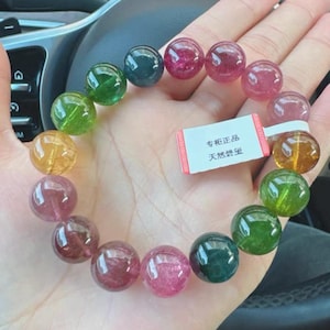Puede incluir: Un brazalete de piedras preciosas multicolores con cuentas redondas en tonos verdes, rosas y amarillos. El brazalete está hecho de piedras preciosas naturales y tiene una etiqueta que dice "Piedra preciosa natural auténtica especial".