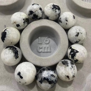 May include: A collection of 10 white and black gemstone beads, each approximately 1.6 cm in diameter. The beads are arranged in a circle on a gray surface.