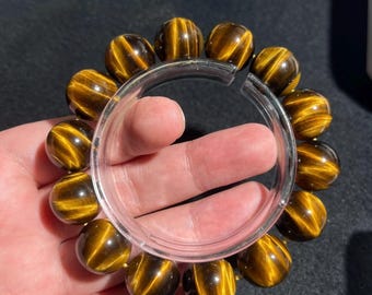 May include: A beaded bracelet featuring round, polished tiger's eye gemstones with characteristic golden-brown chatoyant bands. The beads are strung together in a circular arrangement, displaying a reflective, silky luster across their surfaces.