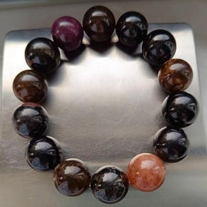 Puede incluir: Un brazalete hecho de cuentas redondas de piedras preciosas negras, marrones y moradas.
