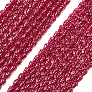 May include: A strand of deep red gemstone beads in a teardrop shape. The beads are smooth and polished, with a glossy finish.
