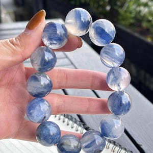 Könnte beinhalten: Ein Armband aus glatten, runden, durchscheinenden Perlen mit einer Mischung aus klaren und tiefblauen Marmormustern. Die Perlen sind in einer kreisförmigen Formation aufgereiht und zeigen natürliche Variationen in Farbe und Textur.