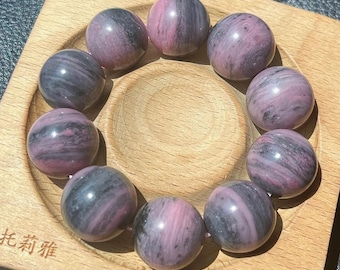 May include: A bracelet made of 10 round, dark pink and black striped beads. The beads are arranged in a circle and are resting on a wooden surface.
