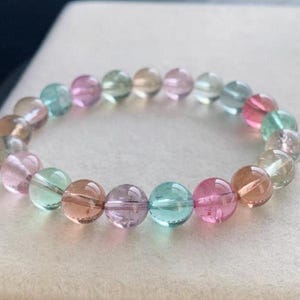 Puede incluir: Un brazalete de cuentas con una variedad de piedras preciosas translúcidas y coloridas. El brazalete incluye cuentas redondas en tonos rosa, verde, azul y marrón. Las cuentas están ensartadas en un cordón elástico transparente.