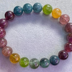 Puede incluir: Un brazalete de piedras preciosas multicolores con cuentas redondas en tonos de rosa, rojo, verde, azul y amarillo.