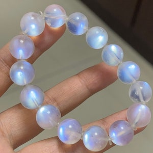 May include: A bracelet made of iridescent white moonstone beads. The beads are round and smooth, and they have a subtle shimmer.