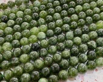 May include: A collection of round, polished green beads arranged in a dense, uniform grid. Each bead displays a unique, semi-translucent appearance with natural internal inclusions, varying shades of forest green, and a smooth, glossy surface finish.