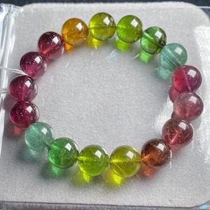 Puede incluir: Una pulsera de cuentas con un espectro de colores, incluyendo rojos profundos, naranjas, verdes y un toque de azul. Las cuentas redondas son translúcidas, creando un aspecto pulido y elegante. Esta joya es un accesorio vibrante.