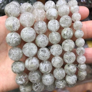 以下が含まれることがあります： 白いルチルクォーツのビーズのネックレス。ビーズは丸く、滑らかで磨かれた仕上げになっています。
