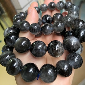 Puede incluir: Tres pulseras de piedras preciosas negras con destellos plateados. Las pulseras están apiladas una encima de la otra y están hechas de cuentas redondas.