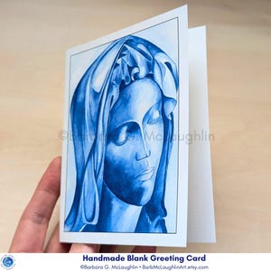 Virgin Mary art card held in the hand, slightly opened to display the inside of the blank greeting card.