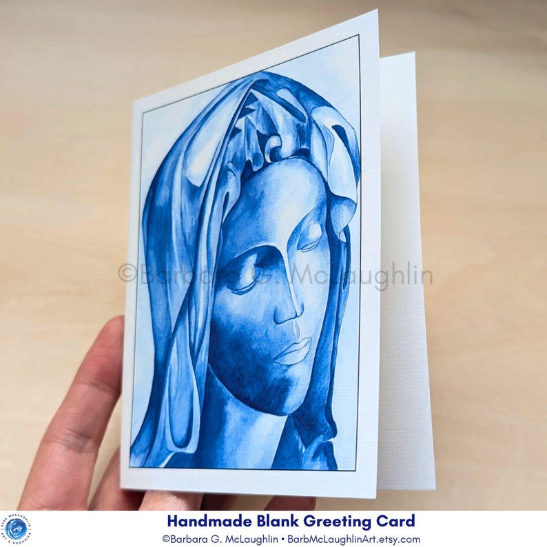 Virgin Mary art card held in the hand, slightly opened to display the inside of the blank greeting card.