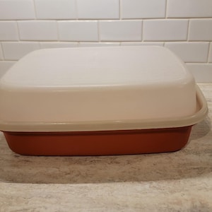 May include: A square, brown plastic container with a white lid. The container is made of a durable plastic and has a smooth finish.