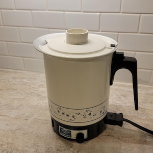 May include: Cream-coloured electric hot pot with a black base and handle. The pot features a floral pattern around the middle and a lid with a central spout. The power cord is black. The text "HOT POT" is visible.