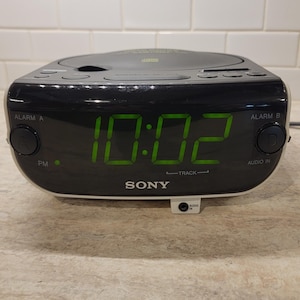 May include: A black and silver Sony CD clock radio with a green digital display showing 10:02. The radio has buttons for alarm, audio in, and track selection.