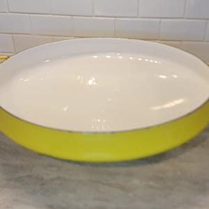 May include: A round, shallow enamelled cast iron braiser pan with a bright yellow exterior and a smooth, cream-coloured interior. The pan features two integrated loop handles on opposite sides, providing a secure grip for lifting and serving.