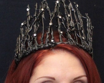 May include: A black crown with a jagged, spiky design and rhinestones. The crown is made of a material that resembles melted plastic.
