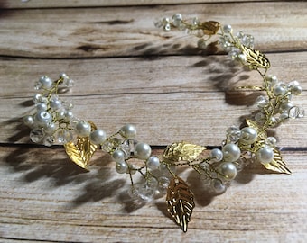 May include: A gold wire headband with white pearls and clear crystals, decorated with gold leaf accents. The headband is designed to resemble a vine with leaves and berries.