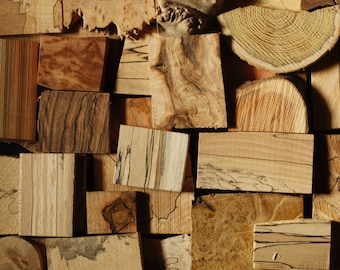 Op de afbeelding: Een verzameling van verschillende stukken hout, elk met unieke nerfpatronen en kleuren. De stukken hout zijn in een willekeurig patroon gerangschikt, waardoor een visueel interessant en getextureerd oppervlak ontstaat.
