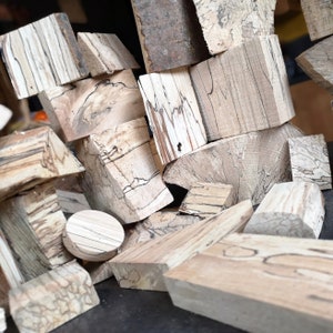 Peut inclure: Une collection de morceaux de bois de différentes tailles et formes avec des motifs de grain uniques. Le bois est brun clair avec des stries et des tourbillons brun foncé. Les pièces sont empilées et disposées de manière aléatoire.