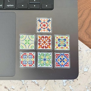 K&ouml;nnte beinhalten: Satz von acht bunten Fliesenaufklebern mit geometrischen Mustern in Rot-, Blau-, Gelb-, Gr&uuml;n- und Wei&szlig;t&ouml;nen. Die Aufkleber sind in zwei Reihen zu je vier auf einem silbernen Laptop angeordnet.