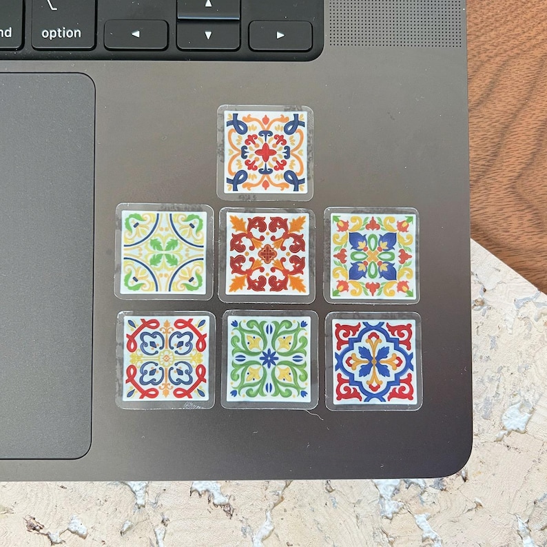 K&ouml;nnte beinhalten: Satz von acht bunten Fliesenaufklebern mit geometrischen Mustern in Rot-, Blau-, Gelb-, Gr&uuml;n- und Wei&szlig;t&ouml;nen. Die Aufkleber sind in zwei Reihen zu je vier auf einem silbernen Laptop angeordnet.