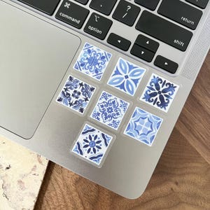 May include: A silver laptop computer with blue and white patterned stickers on the trackpad. The stickers feature a geometric design.