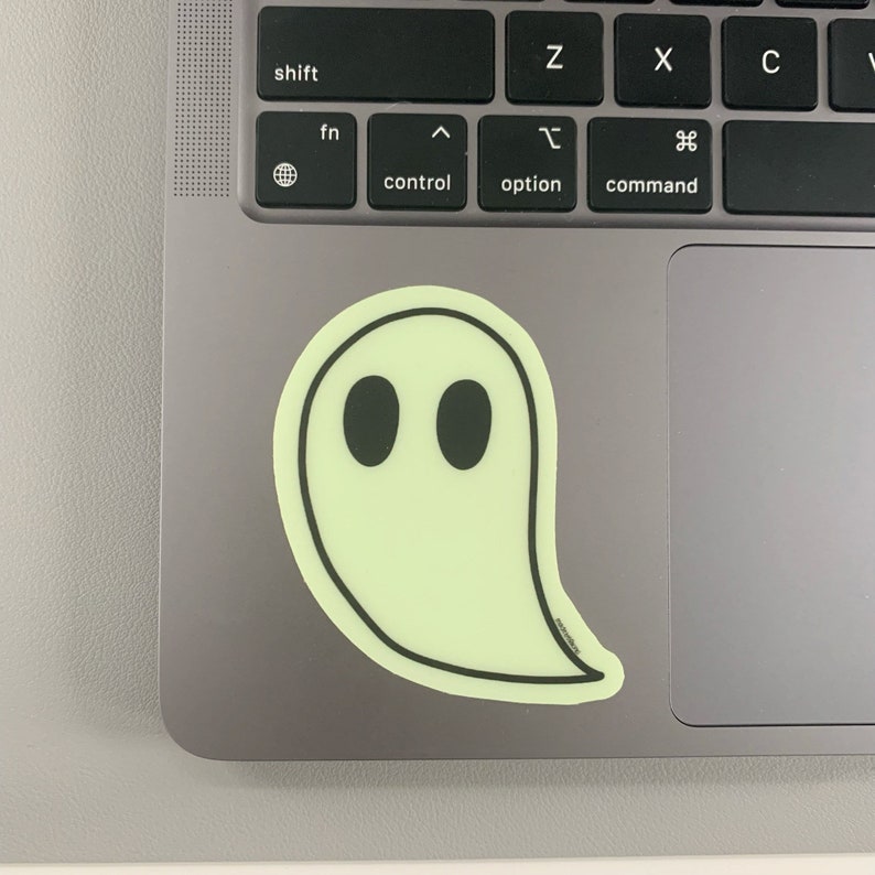 May include: A glow-in-the-dark ghost sticker with black eyes on a gray laptop.