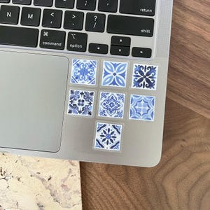 May include: A set of eight blue and white patterned tile stickers. The stickers are arranged in two rows of four on a silver laptop.