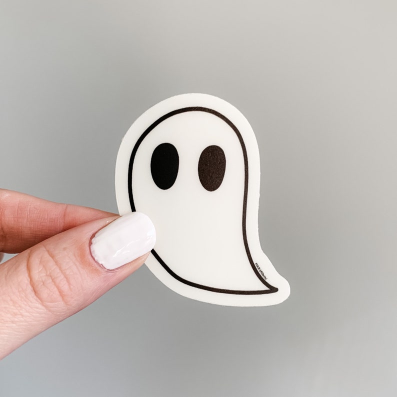 May include: White ghost sticker with black eyes. The sticker is shaped like a ghost with a rounded head and a long, flowing tail.