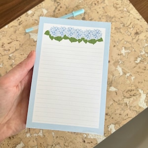May include: A blue lined notepad with a border of light blue and a row of blue hydrangea flowers at the top.